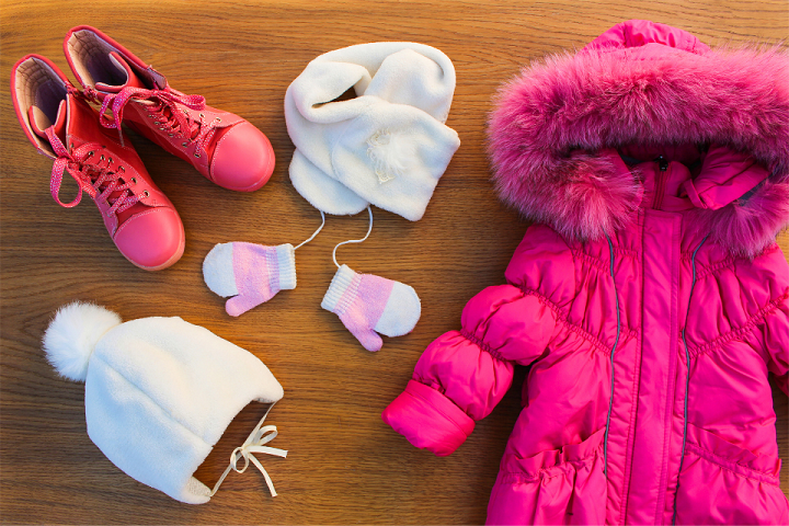 Photo of a pink jacket, boots, scarf, gloves, and hats lying flat on a wooden surface.