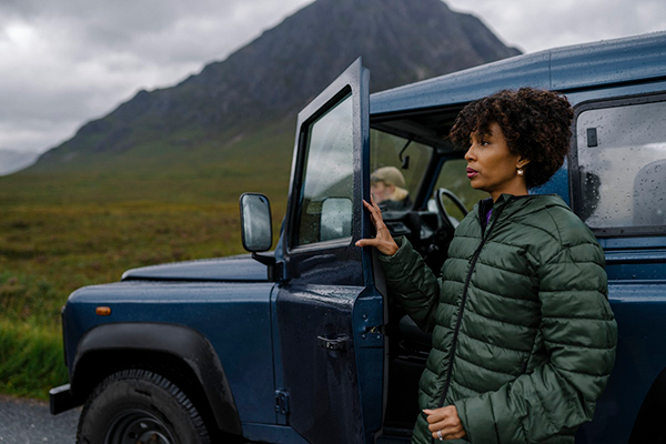 A Black woman stands next to her car