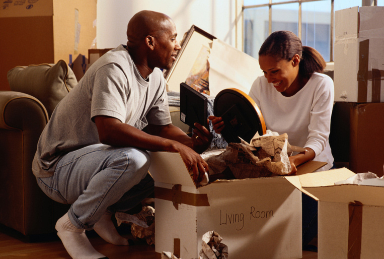 Photo of a Black man and woman unpacking items from a box labeled "Living Room"