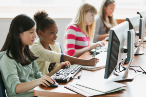 A photo of four teenage girls sitting at a table in front of computers.